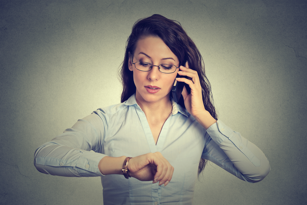 Business and time management concept. Young businesswoman looking at wrist watch, talking on mobile phone running late for meeting.