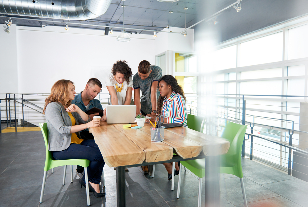 Diverse group of successful creative business people using a laptop during candid meeting