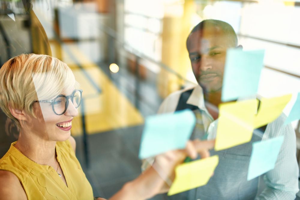 Two creative millenial small business owners working on social media strategy brainstorming using adhesive notes in windows