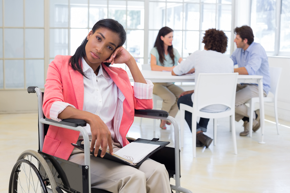 Woman with disability frowning with coworkers are in background in the office