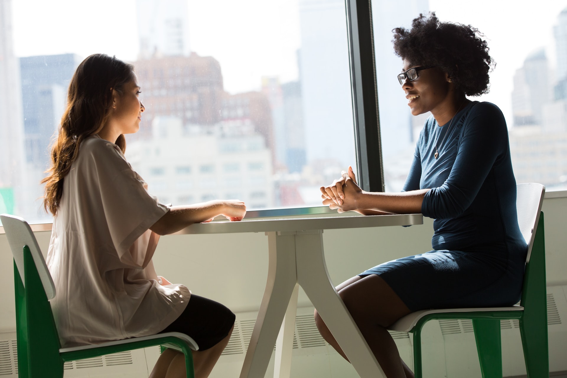 two people talking at a small table near a window wearing business casual