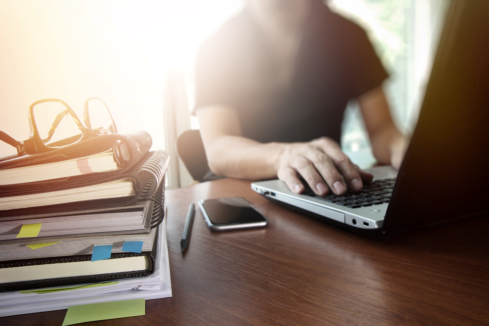 designer hand working with digital tablet and laptop and notebook stack and eye glass on wooden desk in office