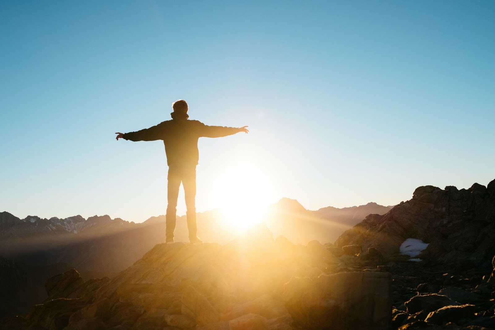 Person facing a sunrise with their arms outstretched, photo by Pablo Heimplatz, sourced from Unsplash